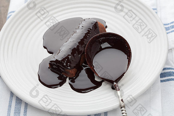 用白色盘子上的复古银汤匙拍摄覆盖着黑色融化巧克力的甜管特写