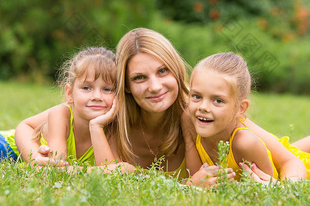 母亲和两个女儿躺在绿草上，看着镜框