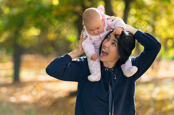 笑着的妈妈让她的小女儿背着小猪，他们一起走过一片多彩的秋天森林
