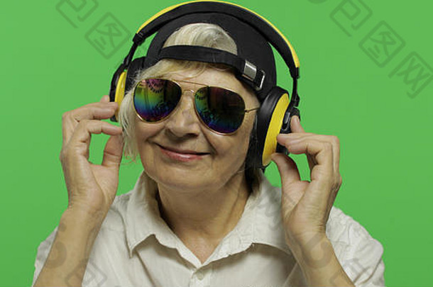 上了年纪的女人听音乐耳机漂亮的快乐祖母太阳镜帽的地方标志文本浓度关键绿色屏幕背景