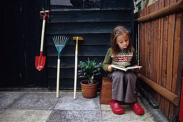 一个小女孩在花园小屋旁独自读书。