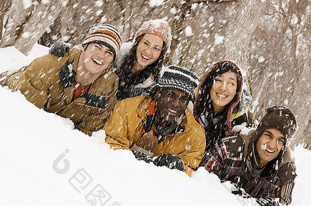 五个年轻人躺在雪地上笑着。下雪了。