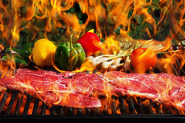 将牛排和蔬菜放在带火焰的烧烤架上