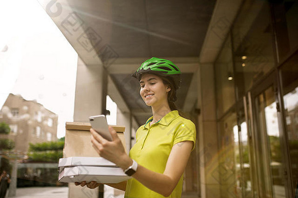 一位身穿黄色衬衫的年轻女子正在运送披萨，她用一些小玩意儿跟踪城市街道上的秩序。使用在线应用程序接收和跟踪发货地址的快递员。现代技术。