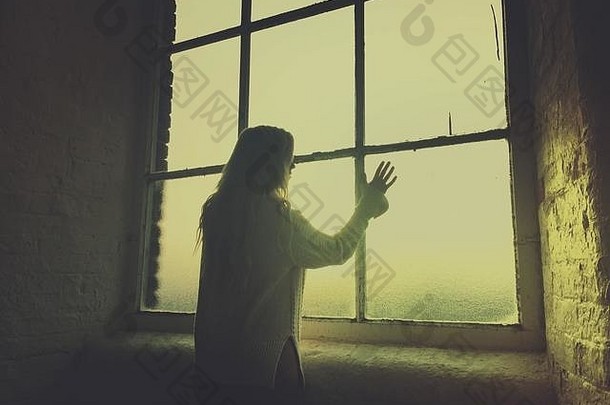 后视图：一名年轻女子的侧影，她看着窗外，手触摸着玻璃