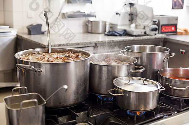 在商业厨房烹饪，大型不锈钢锅在中央燃气灶上装满炖肉和蔬菜