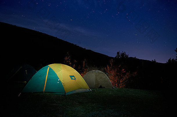 夜晚星空下被照亮的黄色露营帐篷