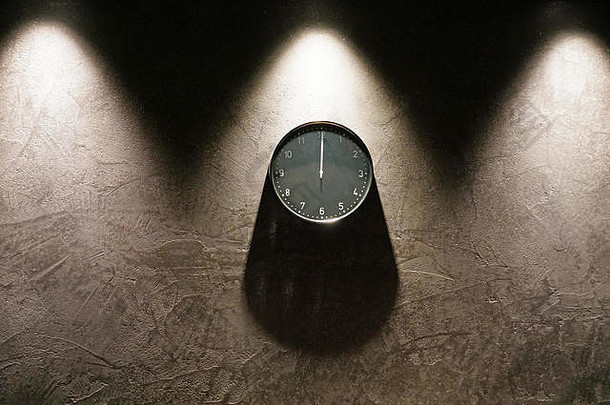 黑色简单模拟时钟，显示午夜，挂在深棕色墙上，周围有空间。上面的两个三角形阴影和一个圆形着色器