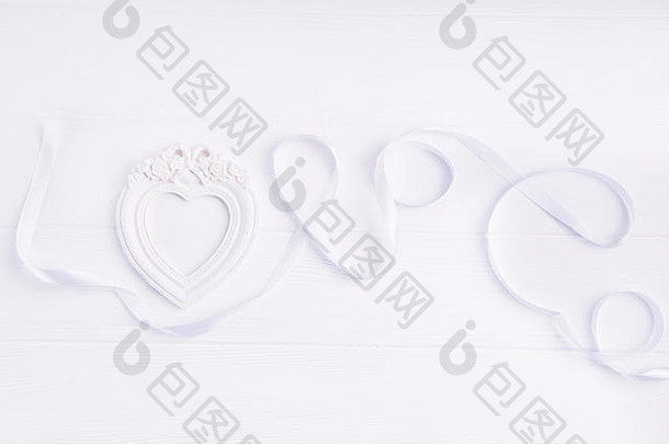 在白色木质背景上，用白色缎带和心形相框书写的俯视爱情文字。平铺。爱的表达。空间。