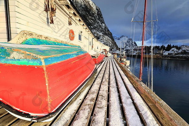 红绿相间的小渔船沿着码头甲板渔港西侧的白色木制仓库<strong>靠岸</strong>。阿克卡维克廷登山背景。哈
