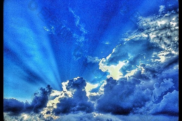 一道道<strong>光柱</strong>穿过<strong>蓝色</strong>天空中的风暴云。照片来源：科林·霍斯金斯。