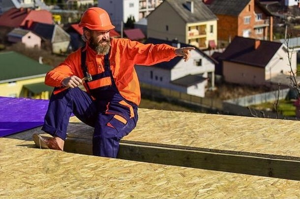 人类建造房屋。平屋顶。屋顶毡。穿着特殊防护服的屋顶工人。在建的新屋顶住宅楼。建筑工人使用锤子。专业维修屋顶。