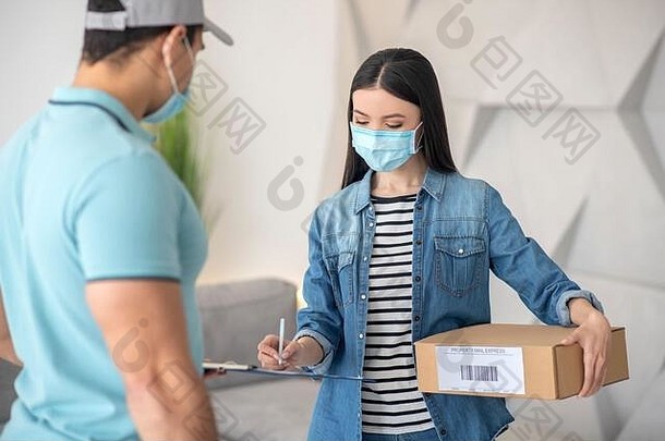 一名妇女拿着包裹在一名男子持有的文件上签名。