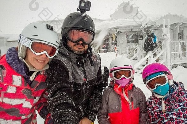 寒假的家人在山坡上自拍。在暴风雪和飓风中，家人和孩子们穿着滑雪服、头盔、滑雪镜。