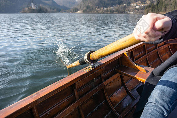 一名年轻女子在一艘木船上划桨，船后有一个小岛流血了——斯洛文尼亚湖流血了，她在木船上划船
