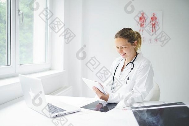 年轻的金发女郎医生坐着实践工作平板电脑检查结果