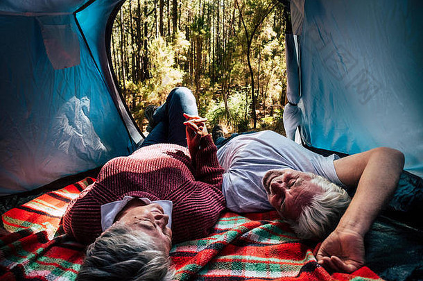 成年老年夫妇躺<strong>在</strong>帐篷里休息，<strong>在</strong>森林里自由野营，以替代旅行和生活方式。爱<strong>永远在</strong>一起的概念