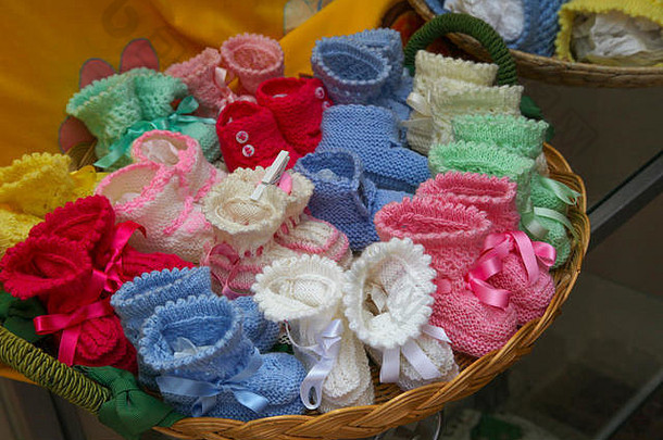 在意大利索伦托的一条后街上，一位老太太手工编织了一个装满婴儿靴的柳条篮子，里面有粉色和蓝色的混合鞋