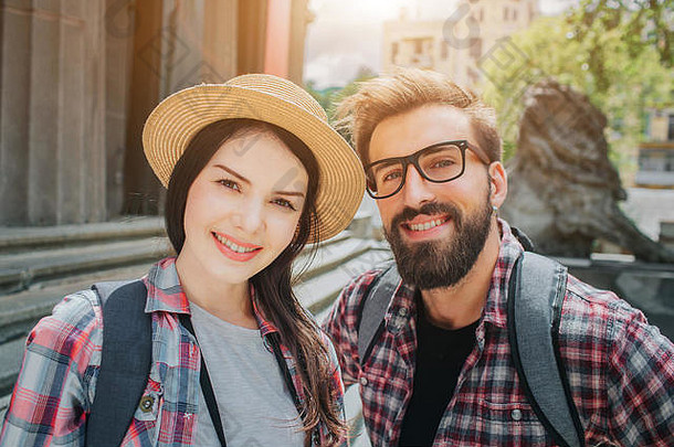 两位年轻游客在照相机前微笑着的美丽照片。男人和女人站在外面靠近楼梯的地方。他们背上有岩石袋。人们是
