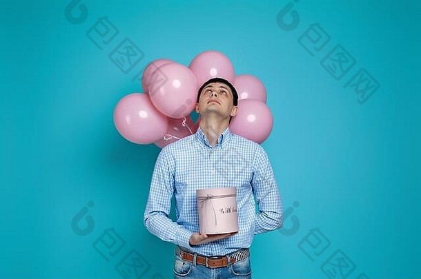 快乐高加索人男人。持有礼物盒子柔和的粉红色的空气气球孤立的蓝色的背景生日聚会，派对