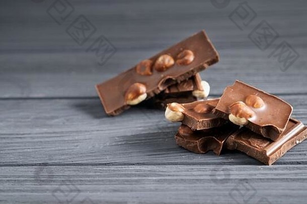 一张灰色的木桌上放着几块带坚果的牛奶巧克力。<strong>榛子</strong>巧克力条。甜褐色巧克力堆。