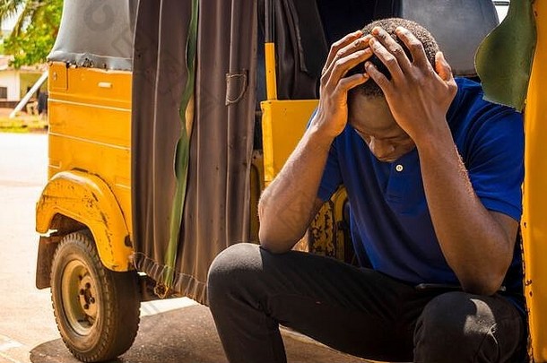 一个年轻<strong>的</strong>非洲男人坐在一辆人力车里，抱着头，看起来很悲伤，感觉很悲伤