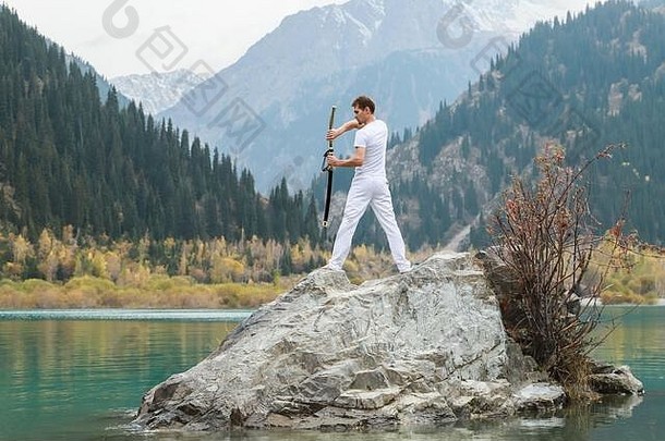 一个年轻人站在一块大石头上，手里拿着一把日本剑