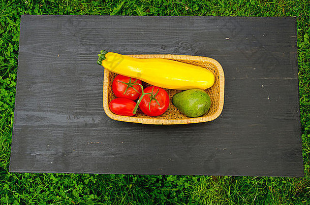 各种各样的蔬菜放在黑色桌子上的木制盘子里。鳄梨、西红柿和西葫芦