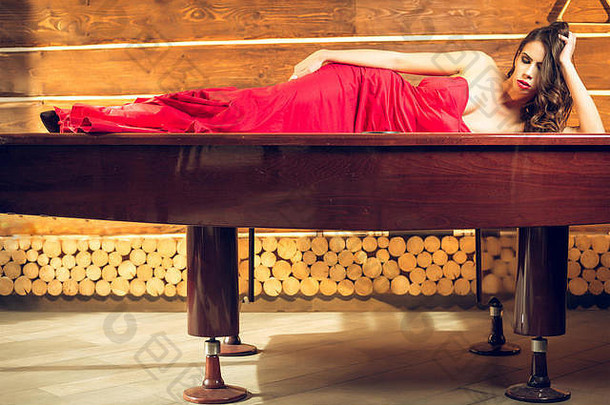 优雅迷人的年轻女子躺在台球桌上，穿着庄严的红色舞会礼服