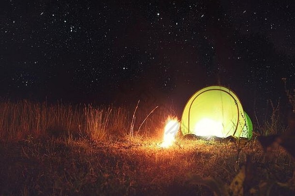 夜晚星空下森林里带篝火的绿色露营帐篷