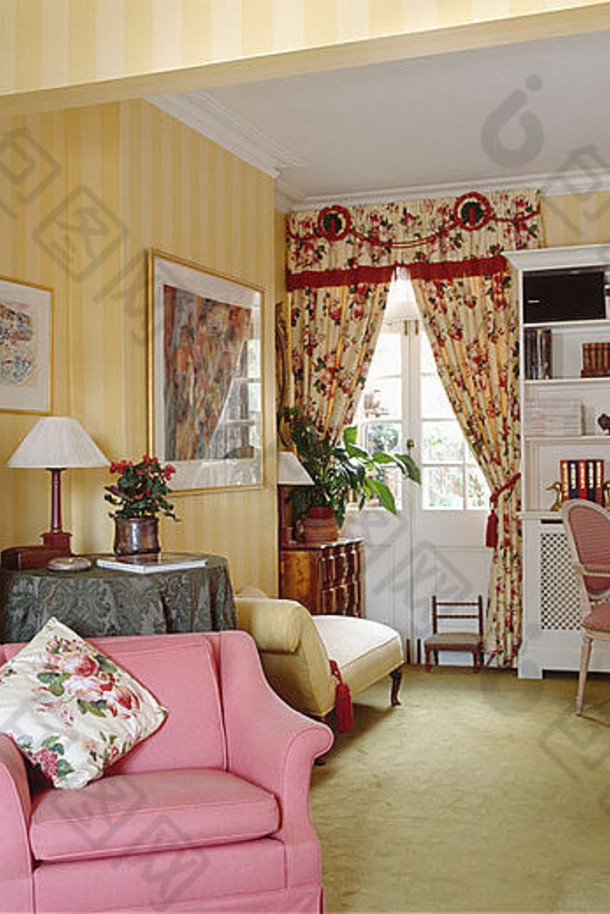 客厅的条纹黄色墙纸和粉红色扶手椅，图案为红色窗帘和淡绿色地毯