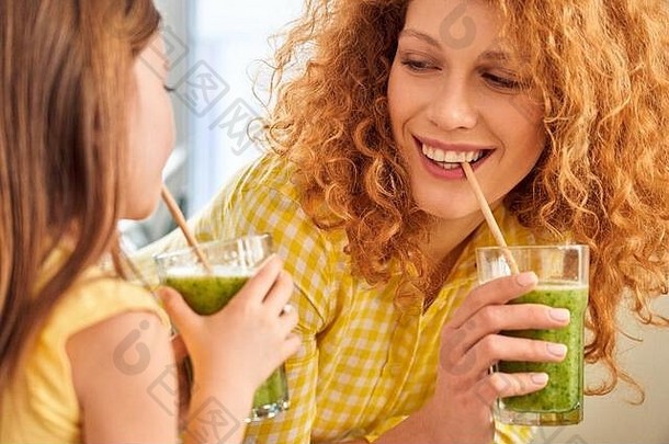 健康饮食。母女俩站在厨房喝着绿色的冰沙，笑着开玩笑的特写镜头