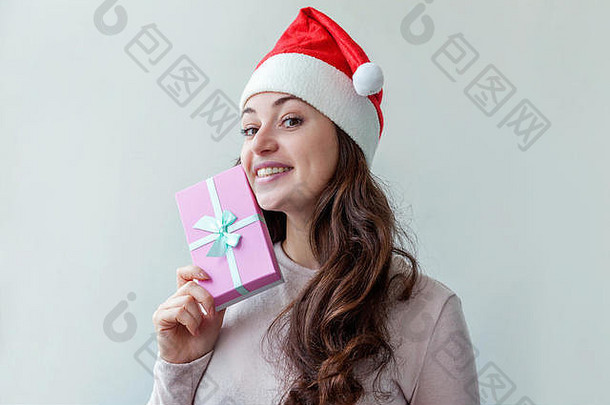 戴着红色圣诞老人帽、留着长发的漂亮女孩，手拿着礼品盒，孤立地放在白色背景上，看上去既高兴又兴奋。年轻女子肖像，真实情感。圣诞快乐，新年快乐