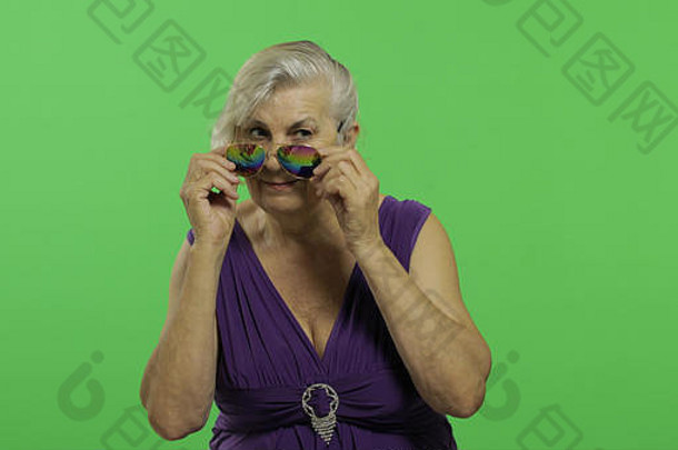 一位戴太阳镜的老妇人微笑着。穿着紫色连衣裙的快乐的老奶奶。放置您的徽标或文字。色度键。绿色屏幕背景