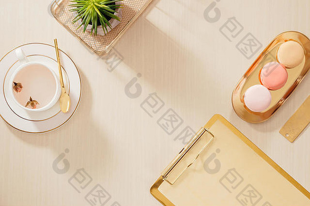 现代金色风格的家庭办公桌，带有文件夹、杏仁饼和咖啡杯，背景为米色。平面布置，俯视生活方式概念`