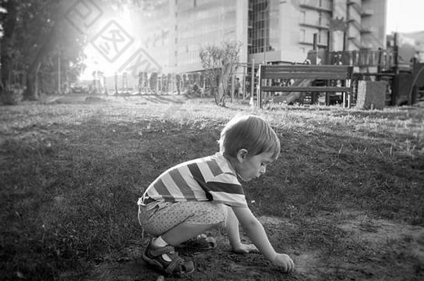 照片可爱的蹒跚学步的男孩坐着公园挖掘沙子