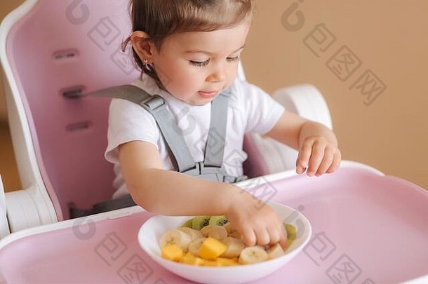 美丽的婴儿女孩时间吃异国情调的水果高椅子可爱的婴儿女孩味道Delitiousfruist芒果猕猴桃你父亲