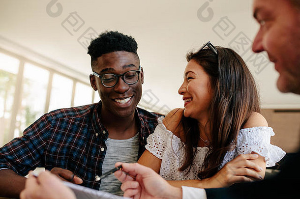 幸福的跨种族夫妇看着他们的新<strong>房屋租赁</strong>协议，微笑着与房地产经纪人交谈。租新房的年轻夫妇。