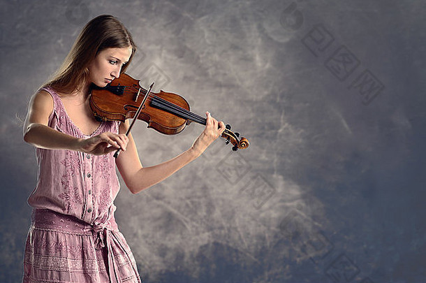 漂亮的年轻的女小提琴家时尚的粉红色的装站玩小提琴经典独奏会学院