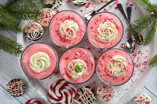 圣诞节免烤草莓芝士蛋糕<strong>慕斯</strong>的特写镜头，上面覆盖着鲜奶油，在玻璃杯中撒上压碎的糖果棒，托盘上有sp
