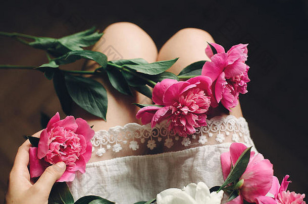 穿着白色波西米亚连衣裙的波西米亚女孩，腿上戴着美丽的粉色牡丹，俯视。文本的空间。手捧鲜花的时髦女人。莫言