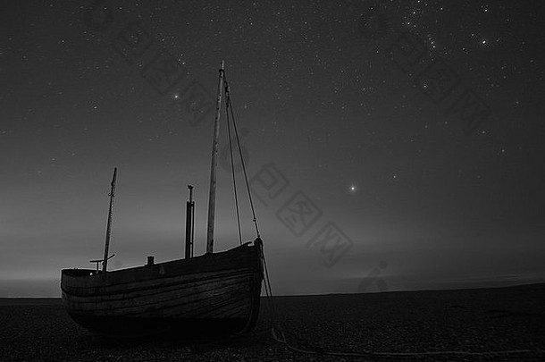 在英国肯特郡的邓格内斯，一艘木船在夜晚的海滩上，被星星覆盖着，黑白相间。