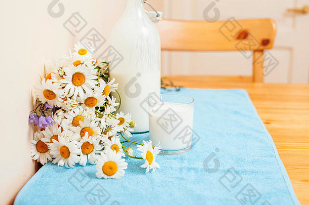 简单时尚的木制厨房，桌上放着一瓶牛奶和玻璃，夏天的花朵甘菊，健康的早晨
