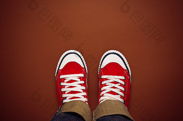从上面的概念来看，穿着红色运动鞋的青少年站在棕色背景上，前面是空白的复印空间，俯视图