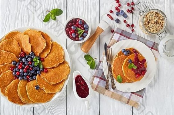 燕麦片薄煎饼配上新鲜蓝莓和蔓越莓，放在白色盘子上，配上蔓越莓酱，俯视水平，平放，免费水疗