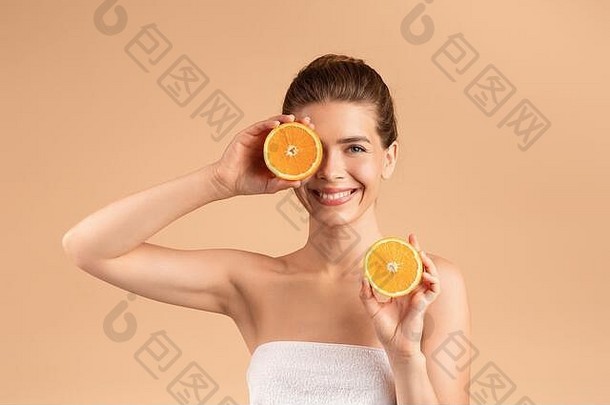 天然皮肤排毒。在米色背景上拿着新鲜橙子片的容光焕发的年轻女孩