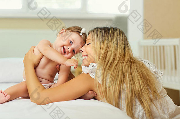 妈妈和宝宝在室内的床上抱着尿布玩耍。