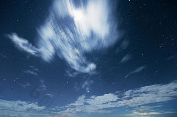 在冬季，有星星的深蓝夜空和移动的云层覆盖着月亮发出的光。