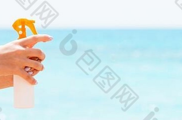 在海滩上，一个女人的手拿着<strong>防晒</strong>霜<strong>喷雾</strong>剂。