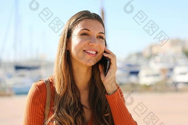 开朗漂亮的年轻女子在打电话，直视前方。在户外，美丽的微笑女孩把智能手机放在耳边。